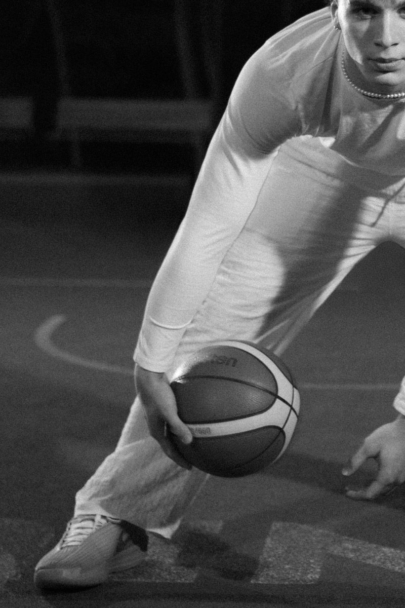 Basketball player mid-dribble in white outfit on outdoor court at night