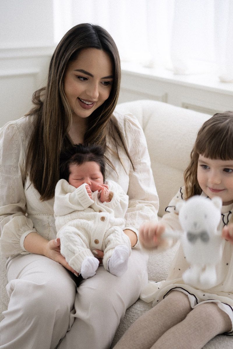 Mother with two daughters and newborn baby sitting together on a cream sofa