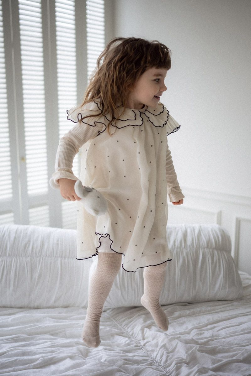 Young girl standing alone in white ruffled dress, studio family photoshoot
