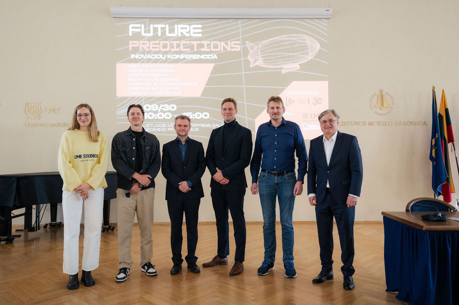 Six conference speakers pose together in front of a Future Predictions presentation screen.