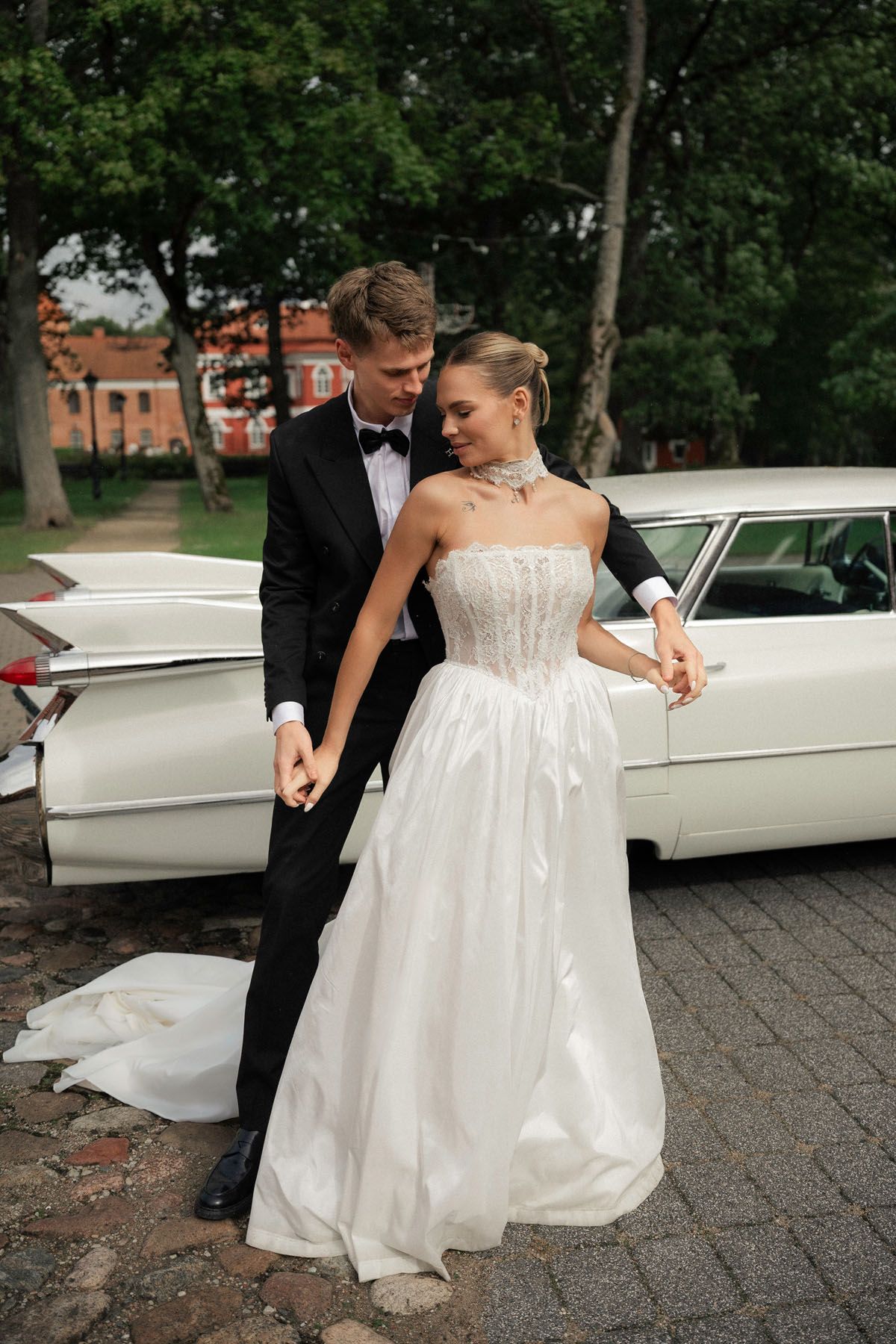 Bride and groom posing beside a vintage car at their Raudondvaris wedding