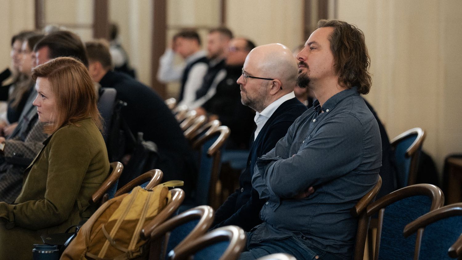 Audience members seated in blue chairs listen to a presentation at a European innovation conference.
