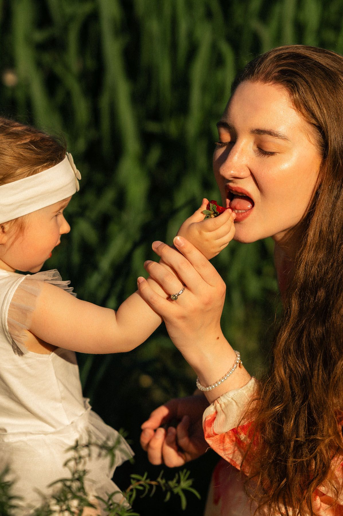 Mother feeding strawberry to toddler daughter, close-up outdoor portrait