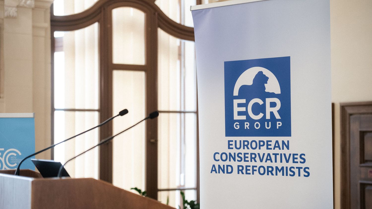 ECR Group European Conservatives and Reformists banner stands beside a podium with microphones in a historic conference hall.