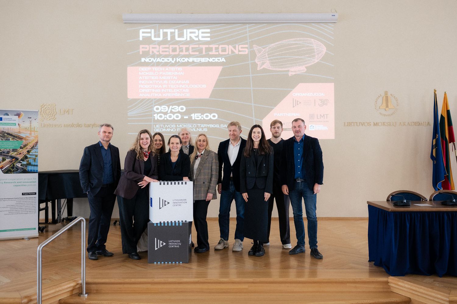 A group of professionals poses on a stage in front of a screen reading Future Predictions at a conference.