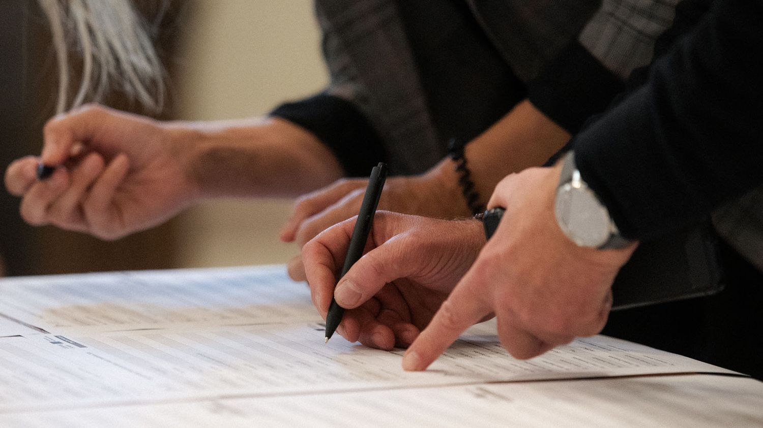 Close-up of several hands holding pens and signing documents on a registration table.