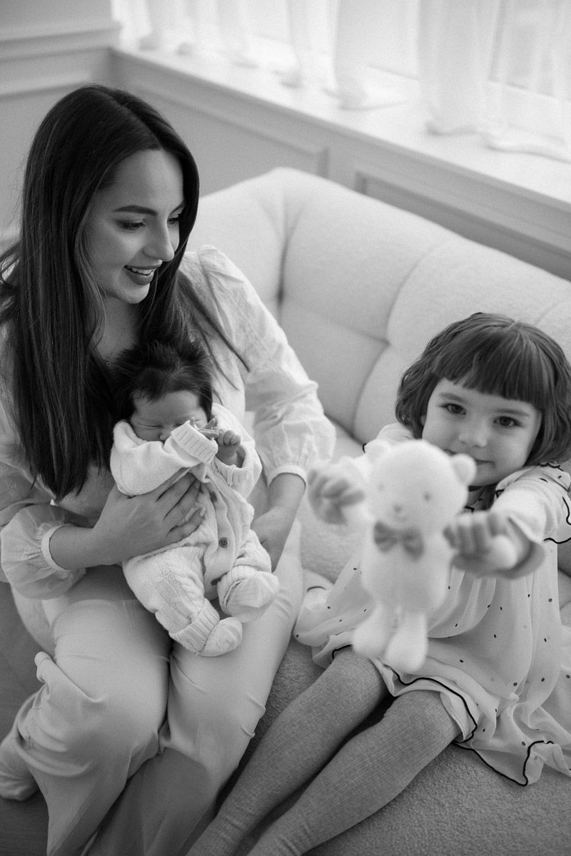 Black and white portrait of mother sitting close with her two daughters and newborn