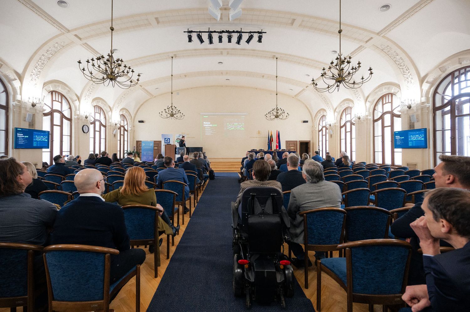 Audience seated in rows in an ornate hall with chandeliers, facing the stage at a Future Predictions event.