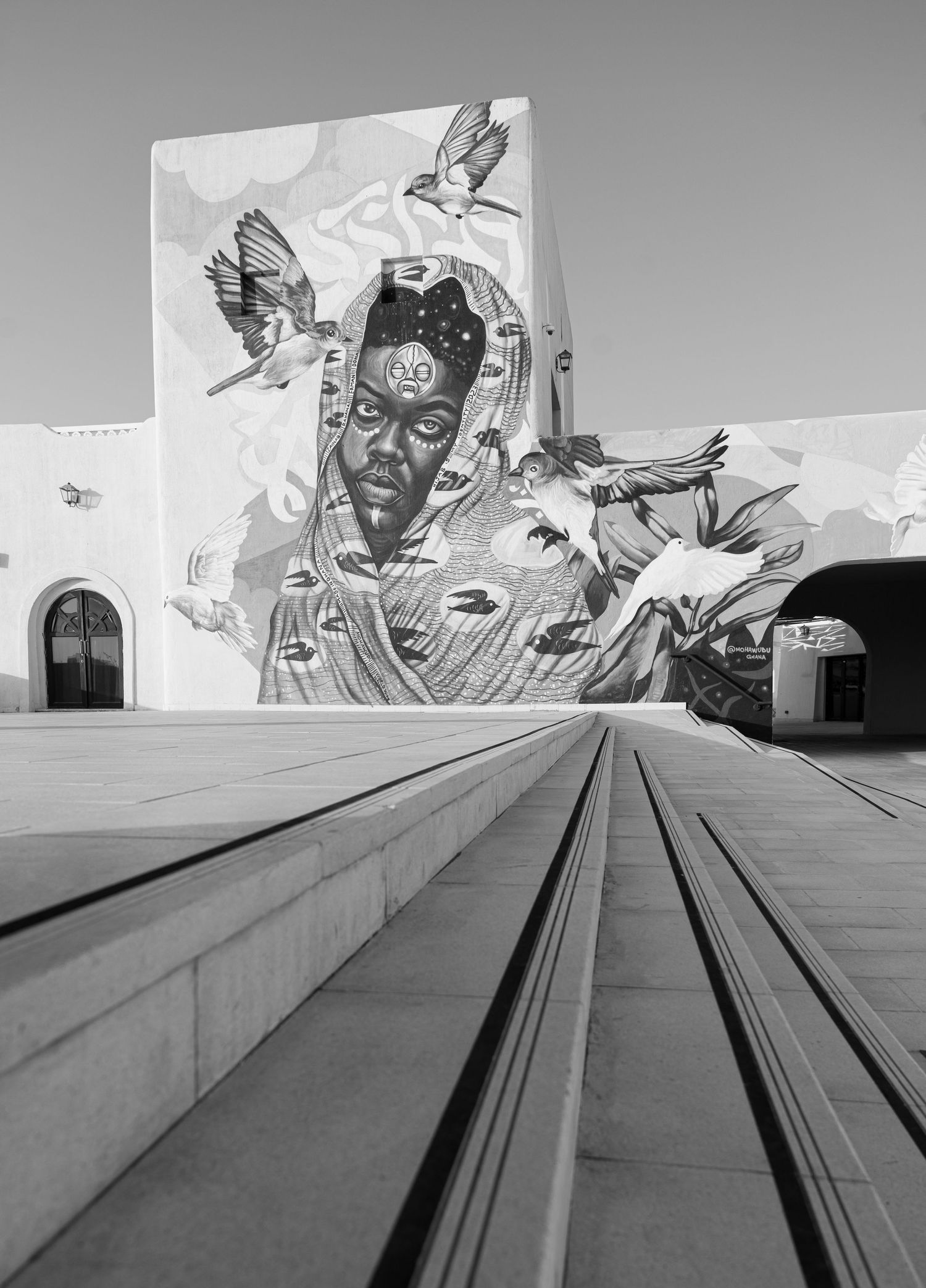 Black and white photo of a large mural featuring a figure surrounded by birds on a building exterior.