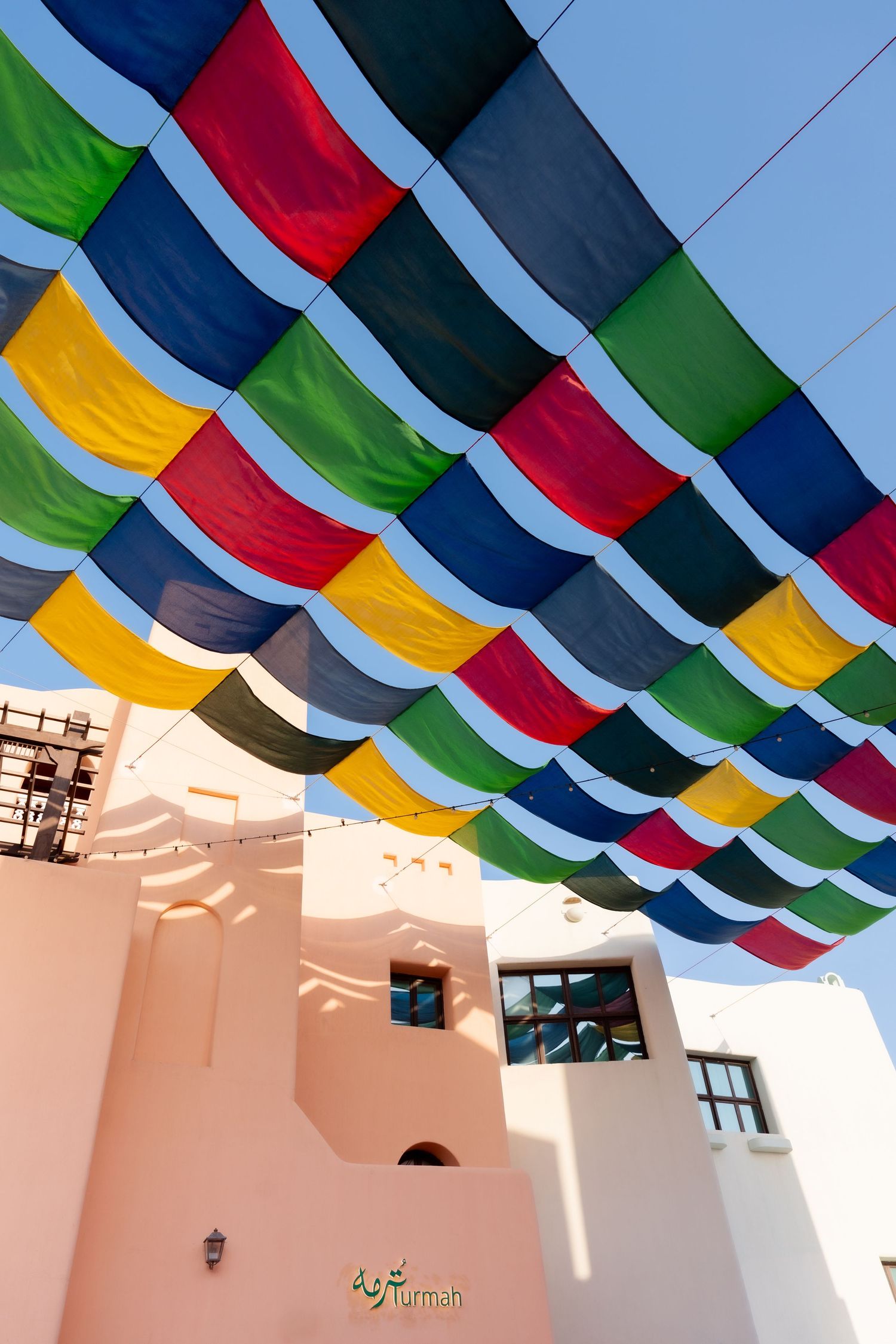 Colorful fabric canopy over traditional Arabic architecture at Turmah restaurant under blue sky.