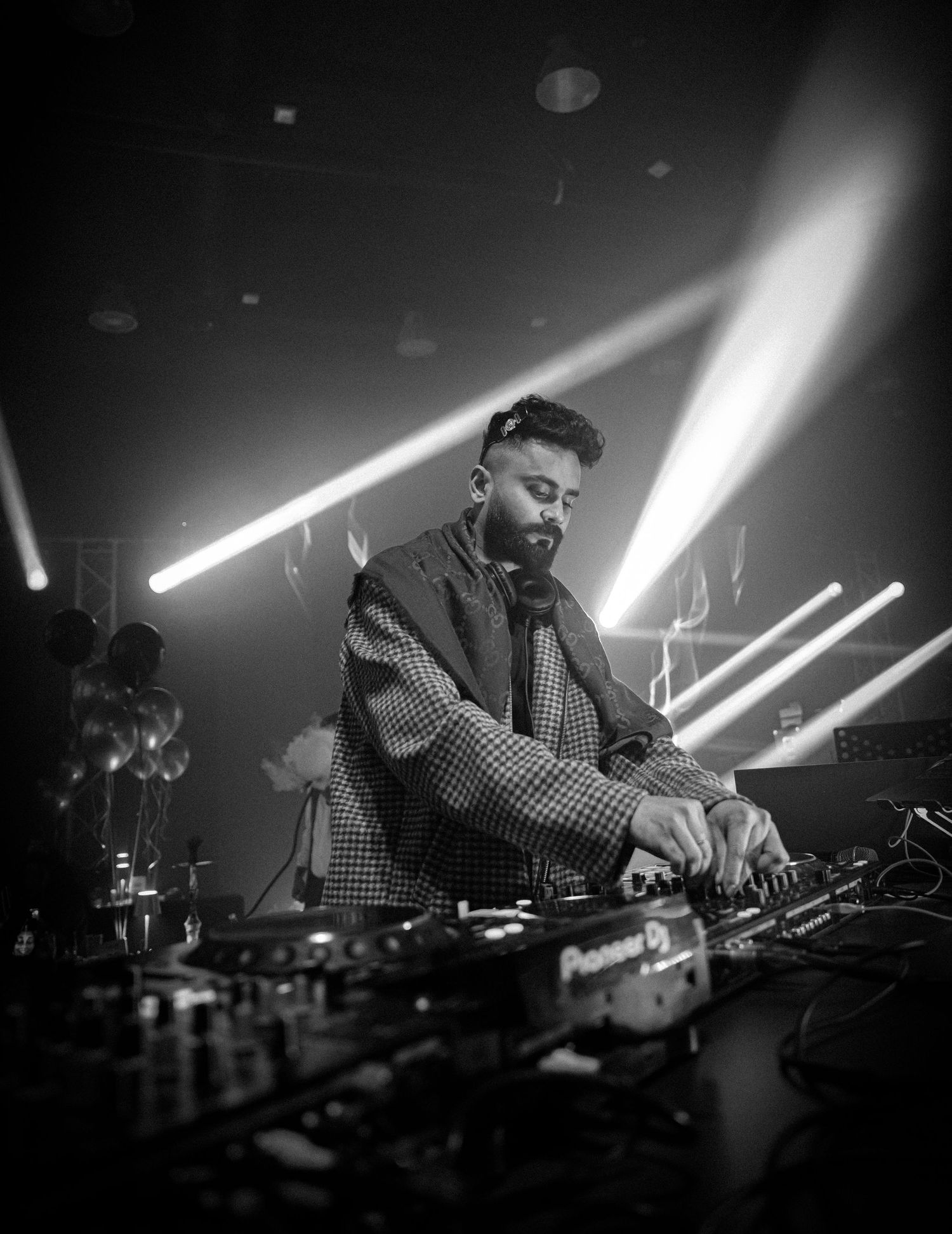 Black and white photo of bearded male DJ performing at Pioneer DJ decks under stage lights.