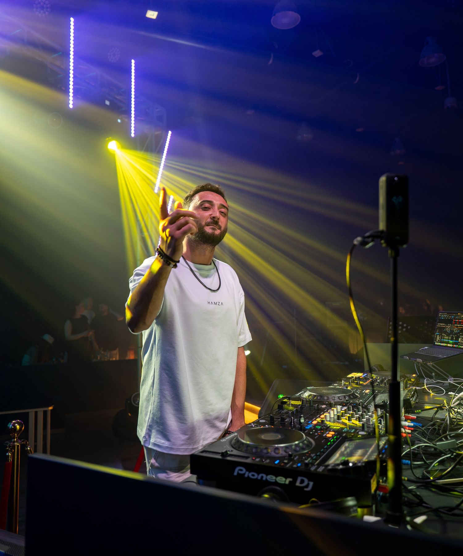 A DJ performs on stage with Pioneer DJ equipment under dramatic yellow stage lighting in a nightclub.
