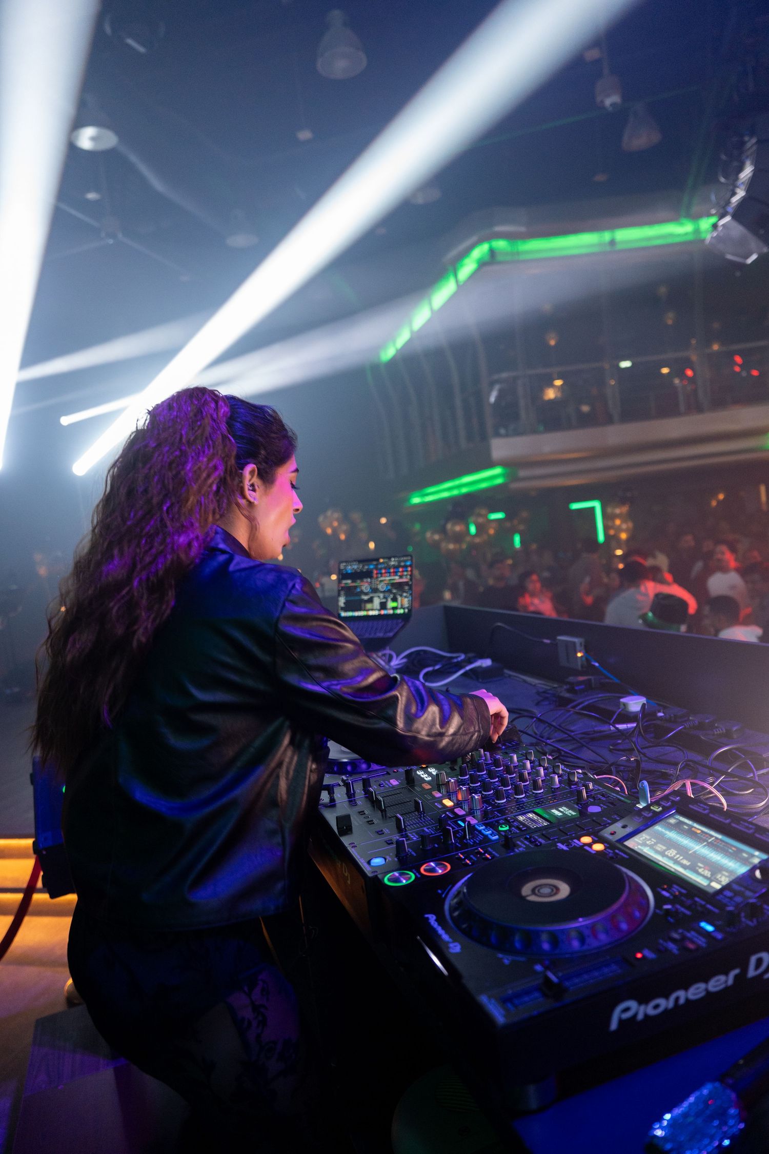 Female DJ performing on Pioneer DJ decks at a nightclub with colorful stage lighting.