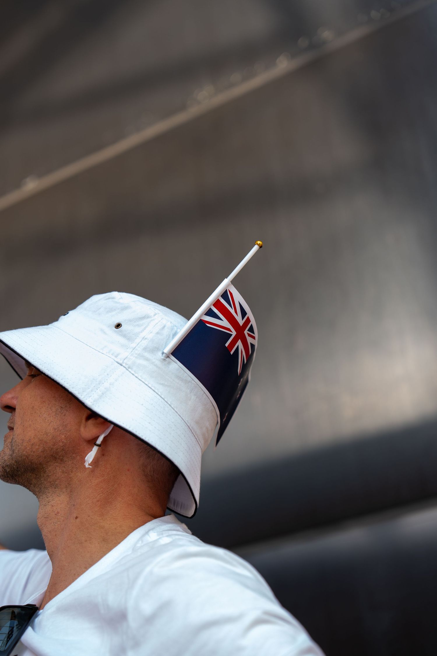Man wearing a white bucket hat with a New Zealand flag pin against a grey background.