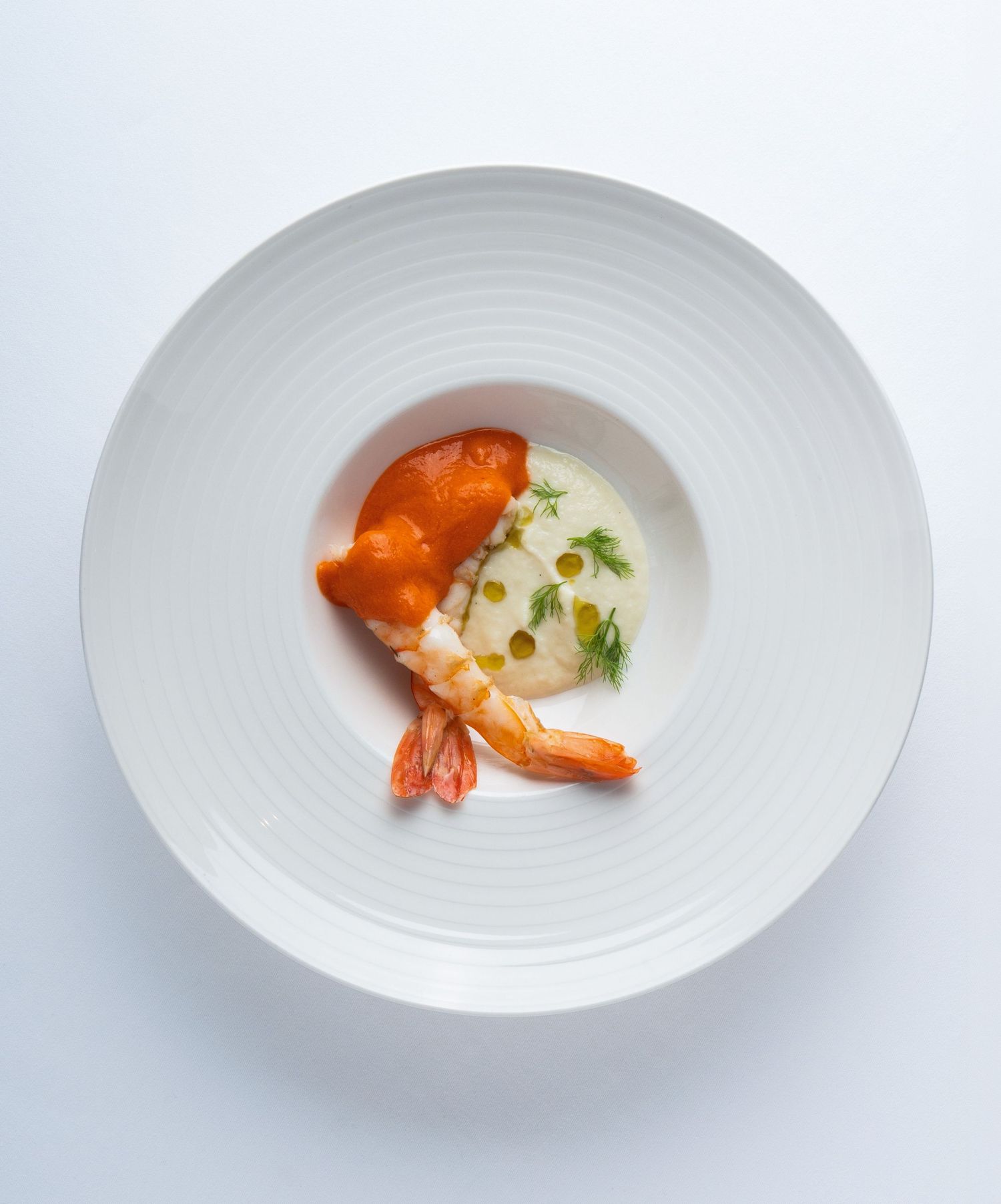 Elegant plated shrimp dish with creamy sauce and capers on a white ridged plate, fine dining presentation.