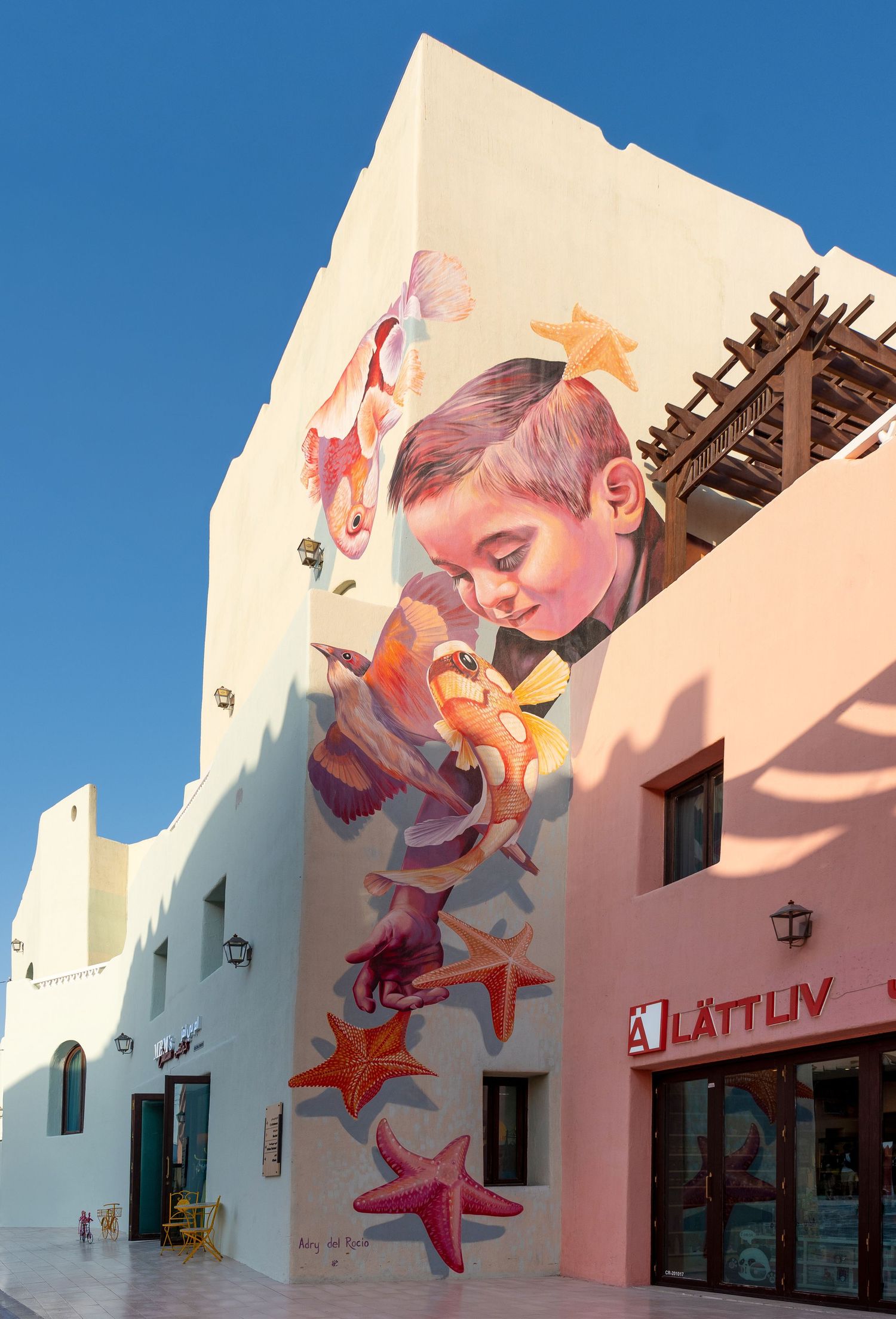 Large colorful street art mural of a child with starfish and sea creatures on a building wall.