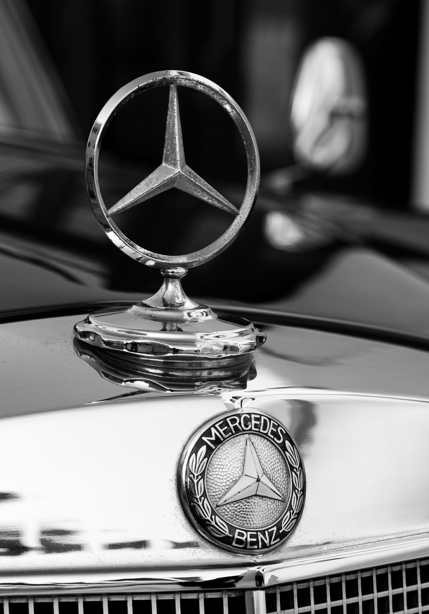 Black and white close-up of a classic Mercedes-Benz hood ornament and emblem on a vintage luxury car.