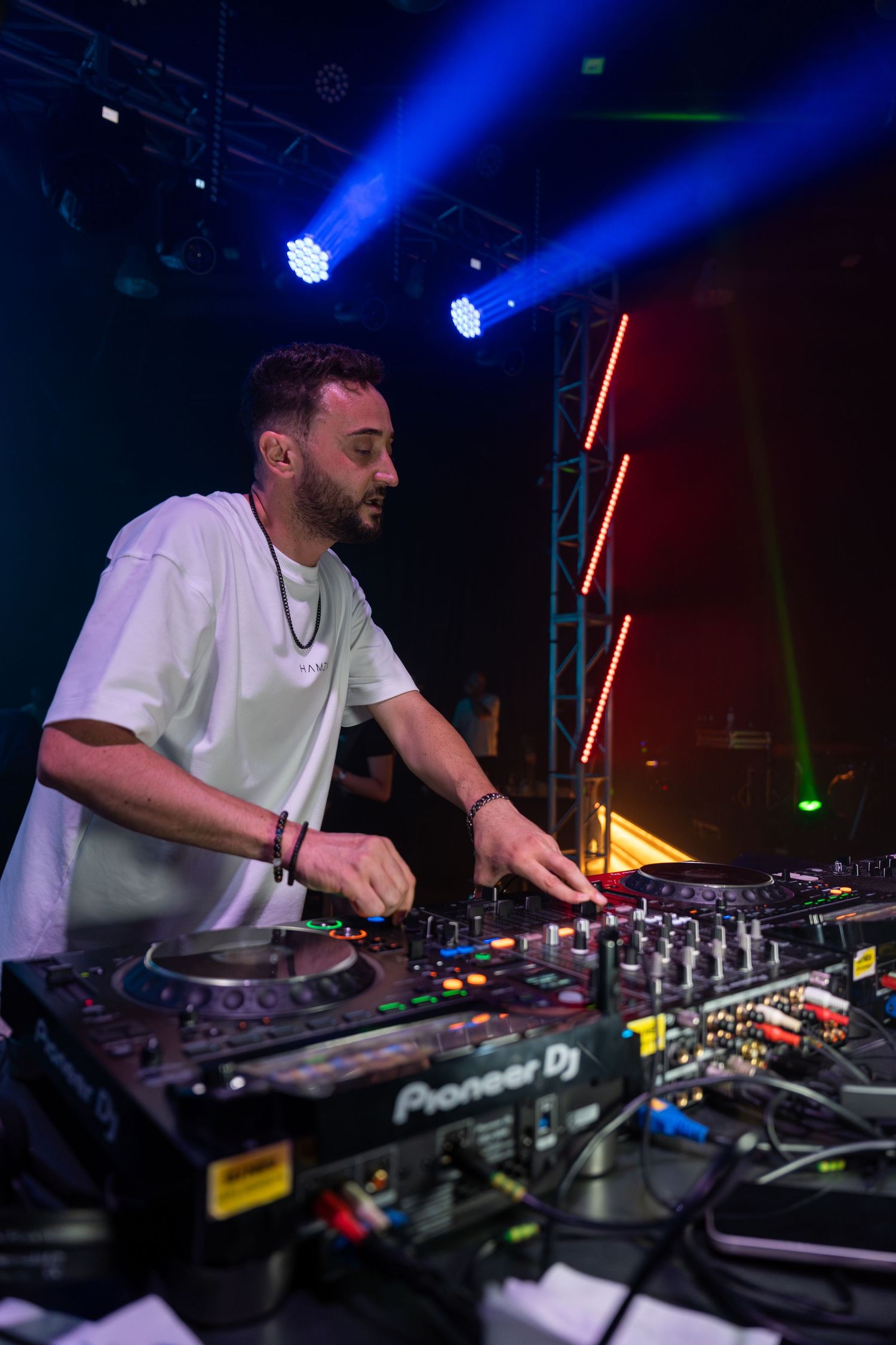 DJ performing on Pioneer DJ equipment under colorful stage lights in a dark nightclub venue.