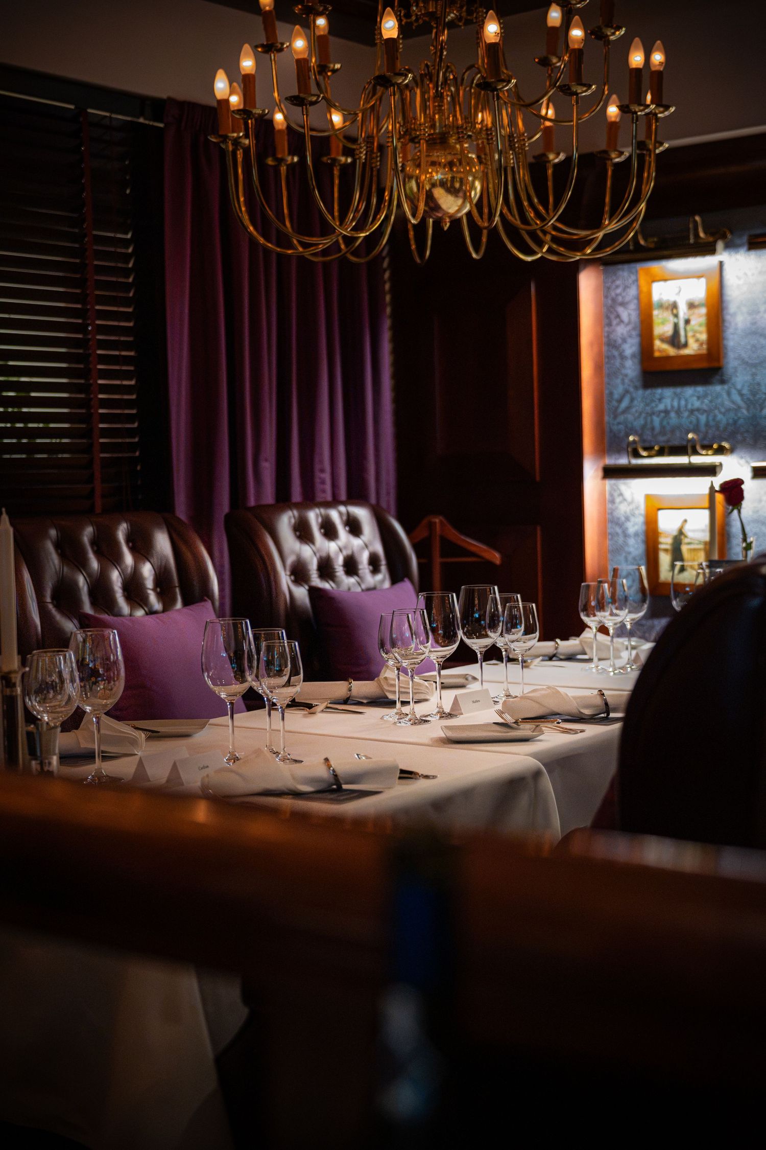 Elegant restaurant private dining room with tufted leather chairs, purple cushions, crystal wine glasses, and ornate chandelier.