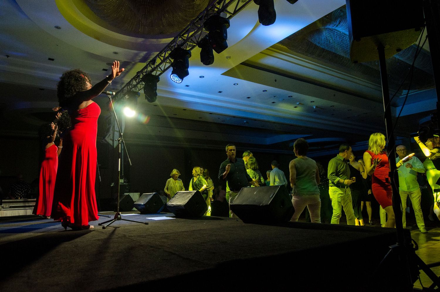 Female singer in red dress performing on stage before a large audience at a grand ballroom event.