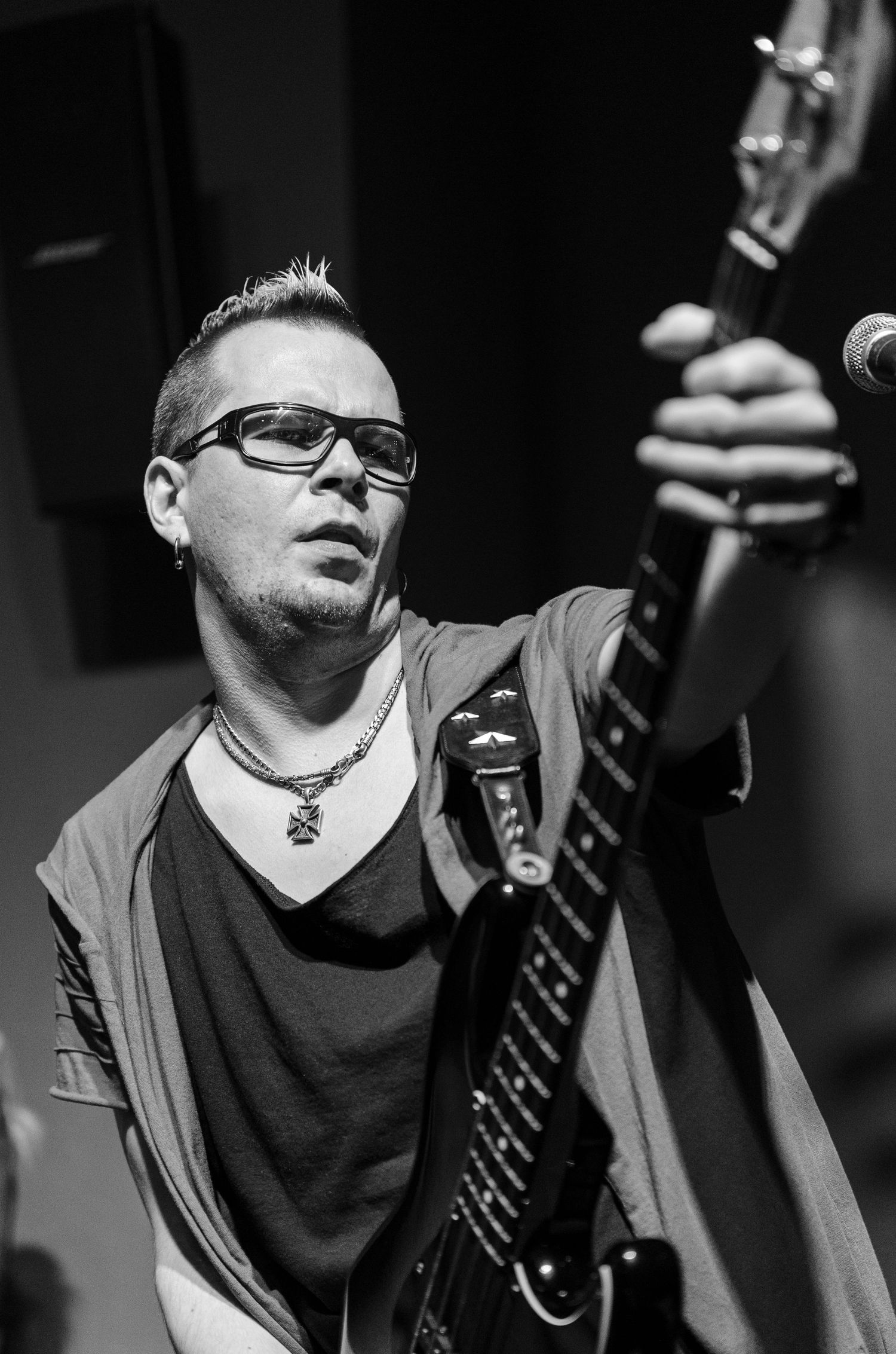 Black and white photo of a male guitarist with glasses and a cross necklace performing on stage.