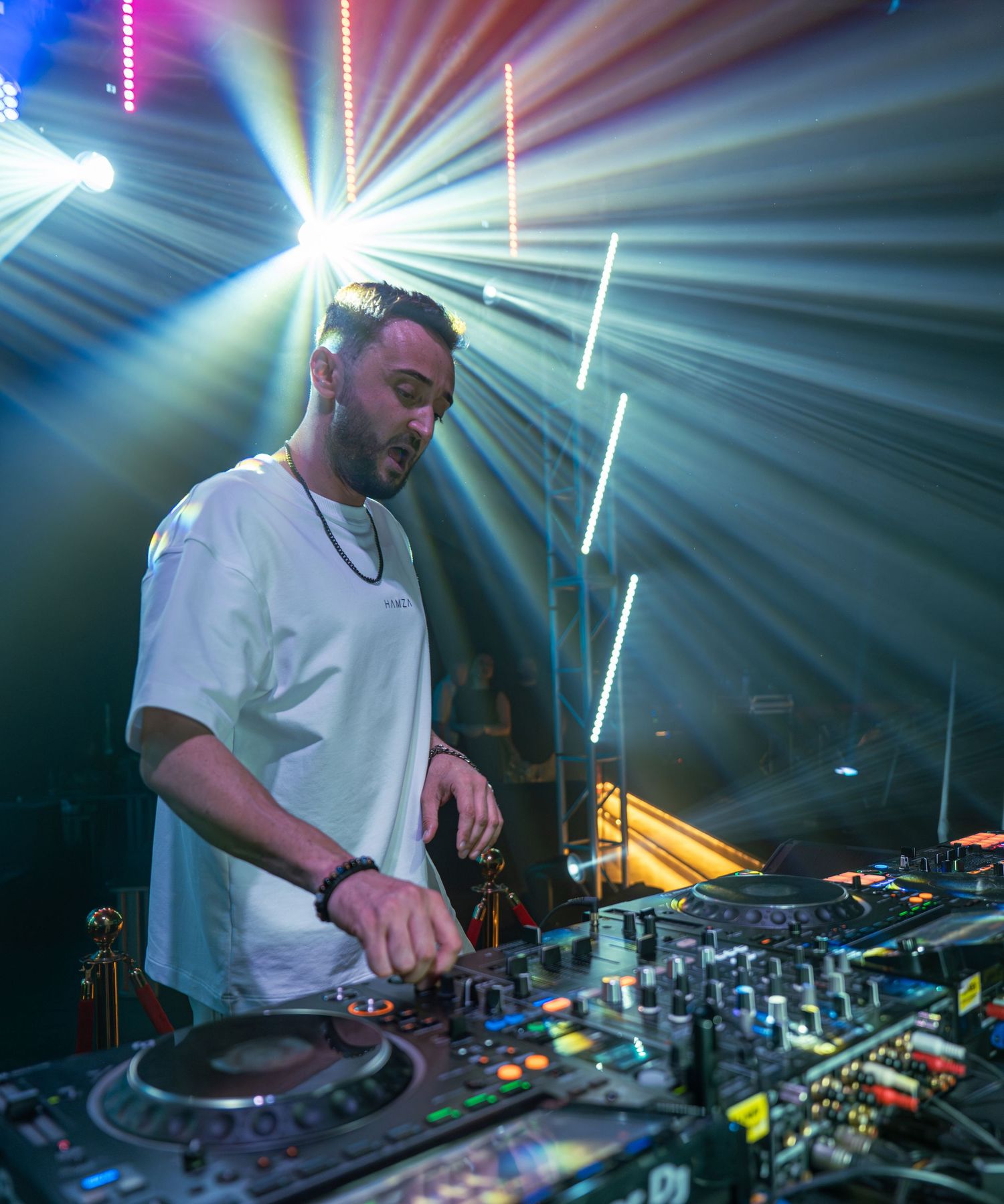 Male DJ mixing music on Pioneer DJ equipment under bright stage lights in a nightclub setting.