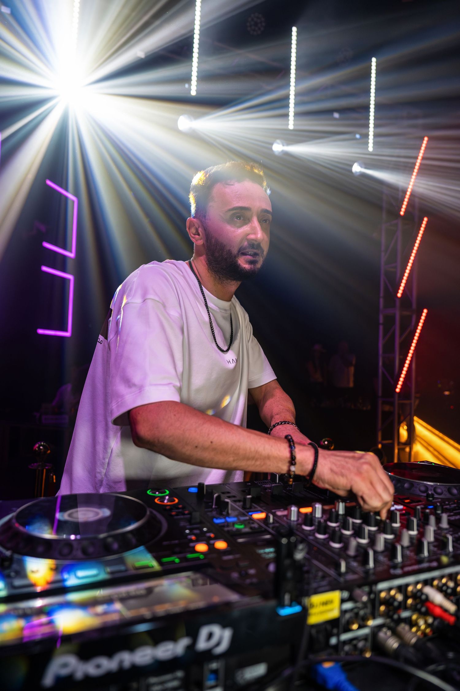 DJ performing at a nightclub with Pioneer DJ equipment under colorful stage lights.