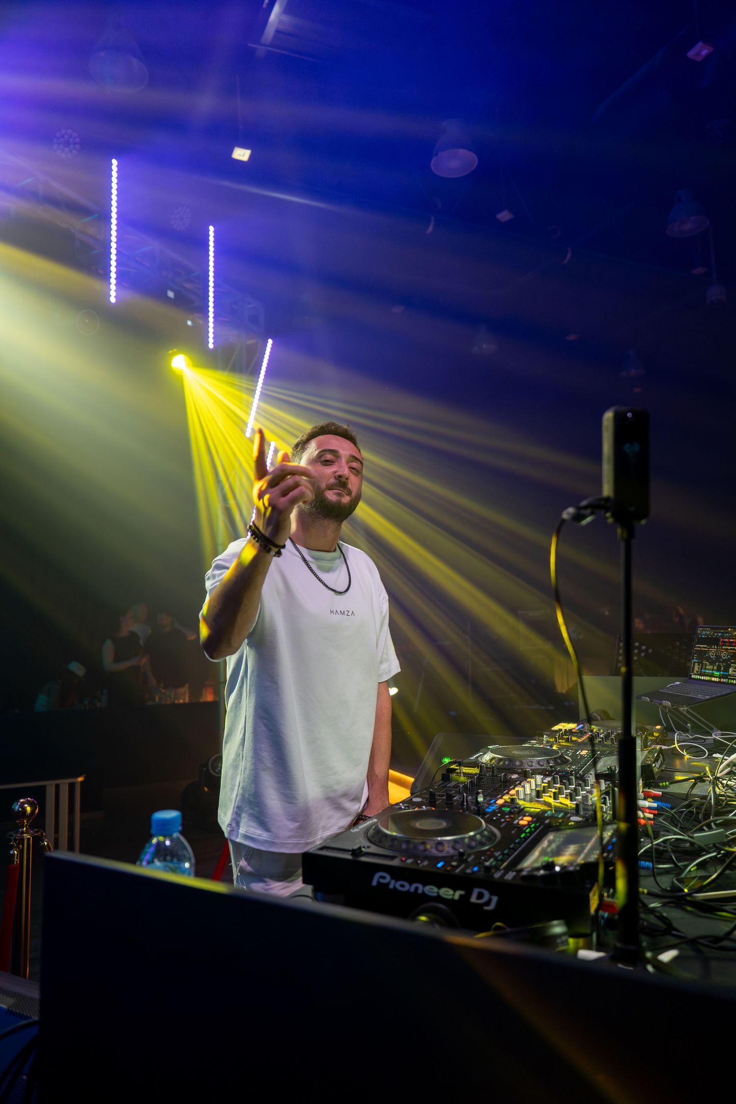 DJ performing at nightclub with Pioneer DJ equipment under dramatic yellow and blue stage lighting.