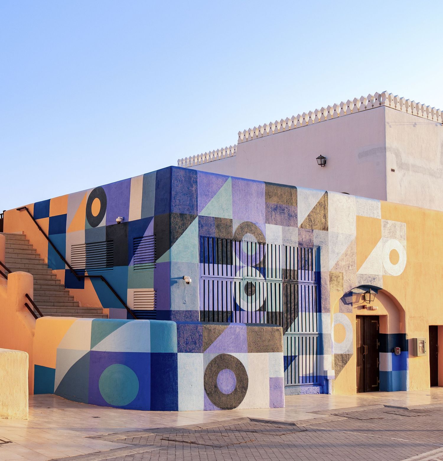 Colorful geometric mural with circles and triangles in blue, orange, and purple on a building exterior.