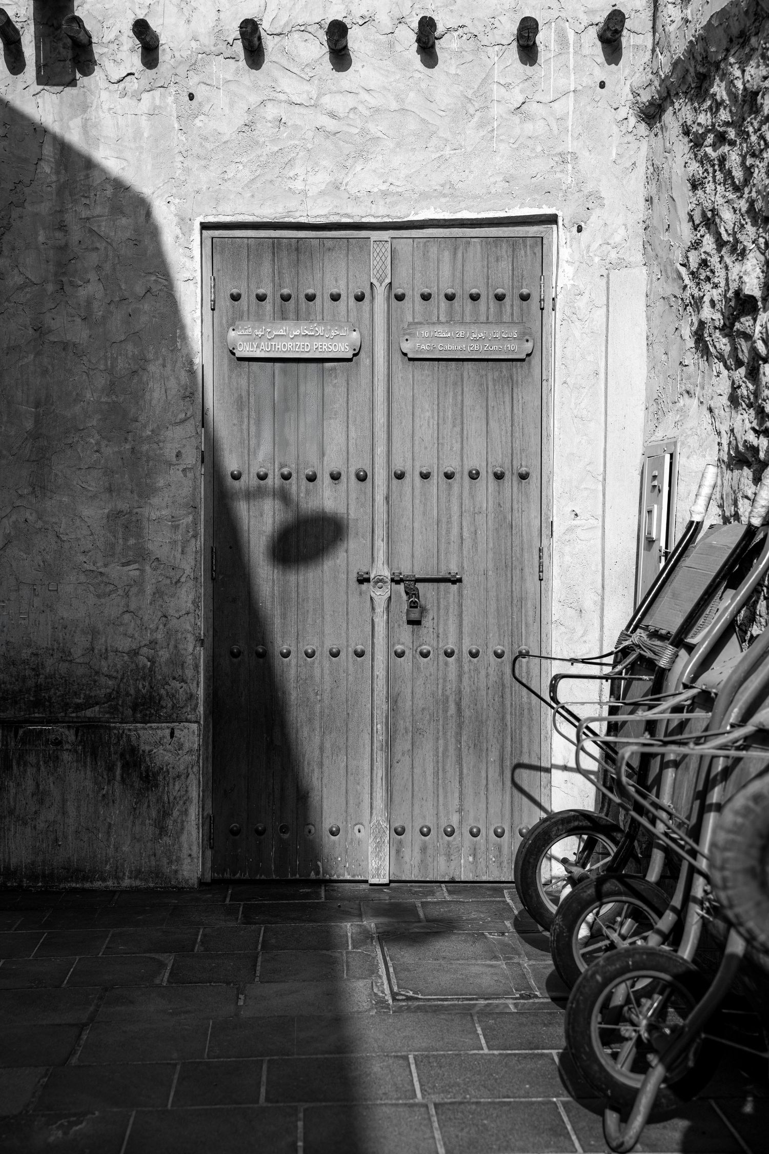 Black and white photo of an ornate wooden door with metal studs and padlock, flanked by bicycles against a textured wall.