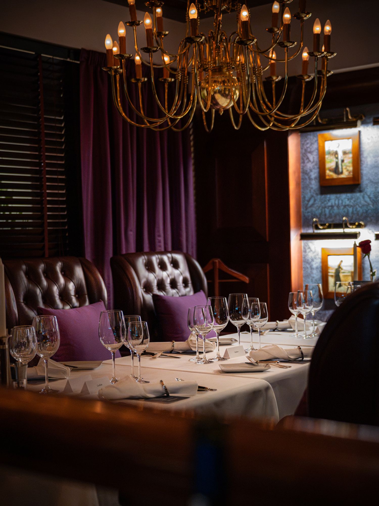 Elegant private dining room with tufted leather chairs, purple cushions, crystal wine glasses, and a gold chandelier overhead.