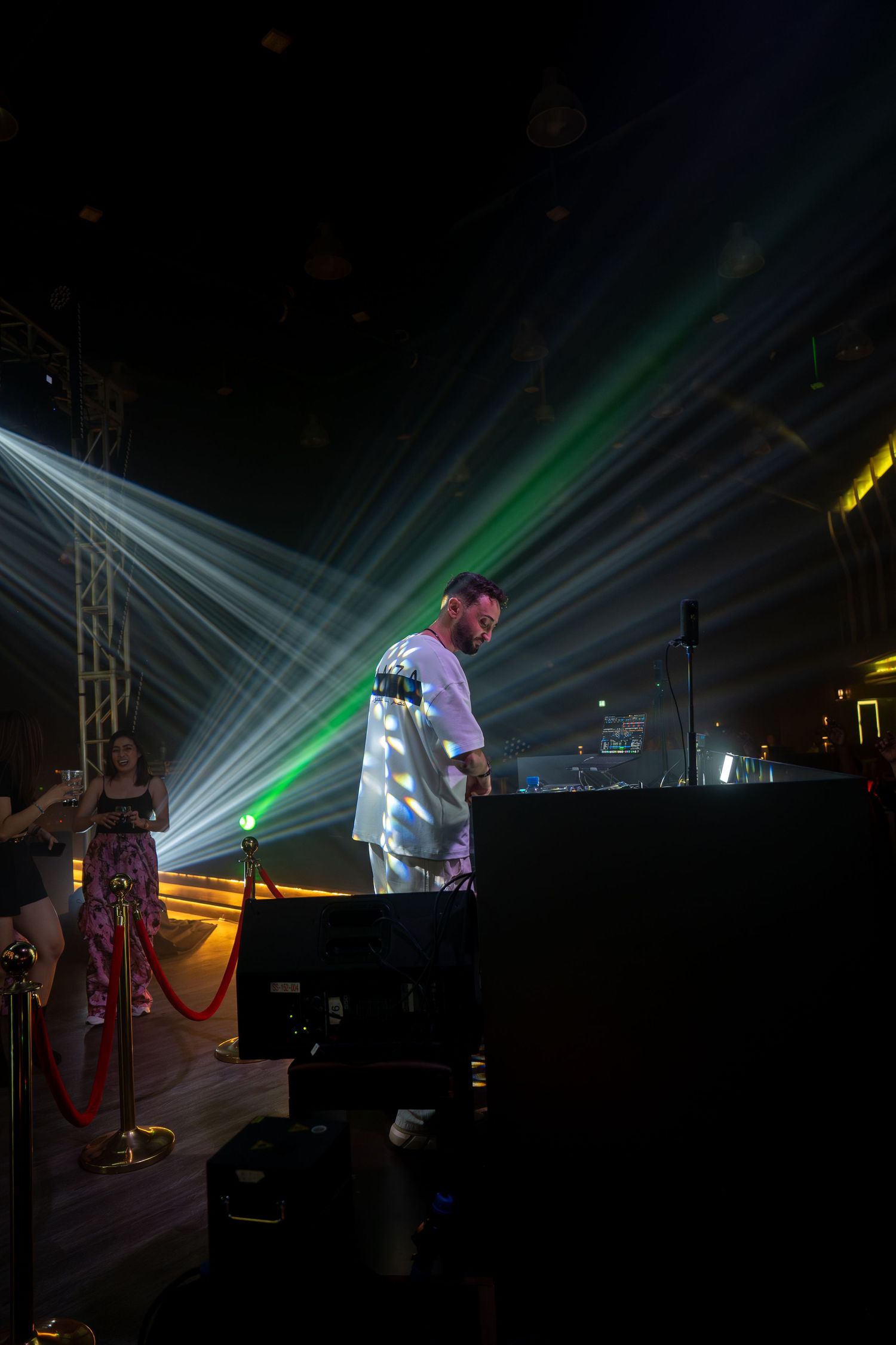 DJ performing at a nightclub with dramatic laser light show beams in green and white overhead.