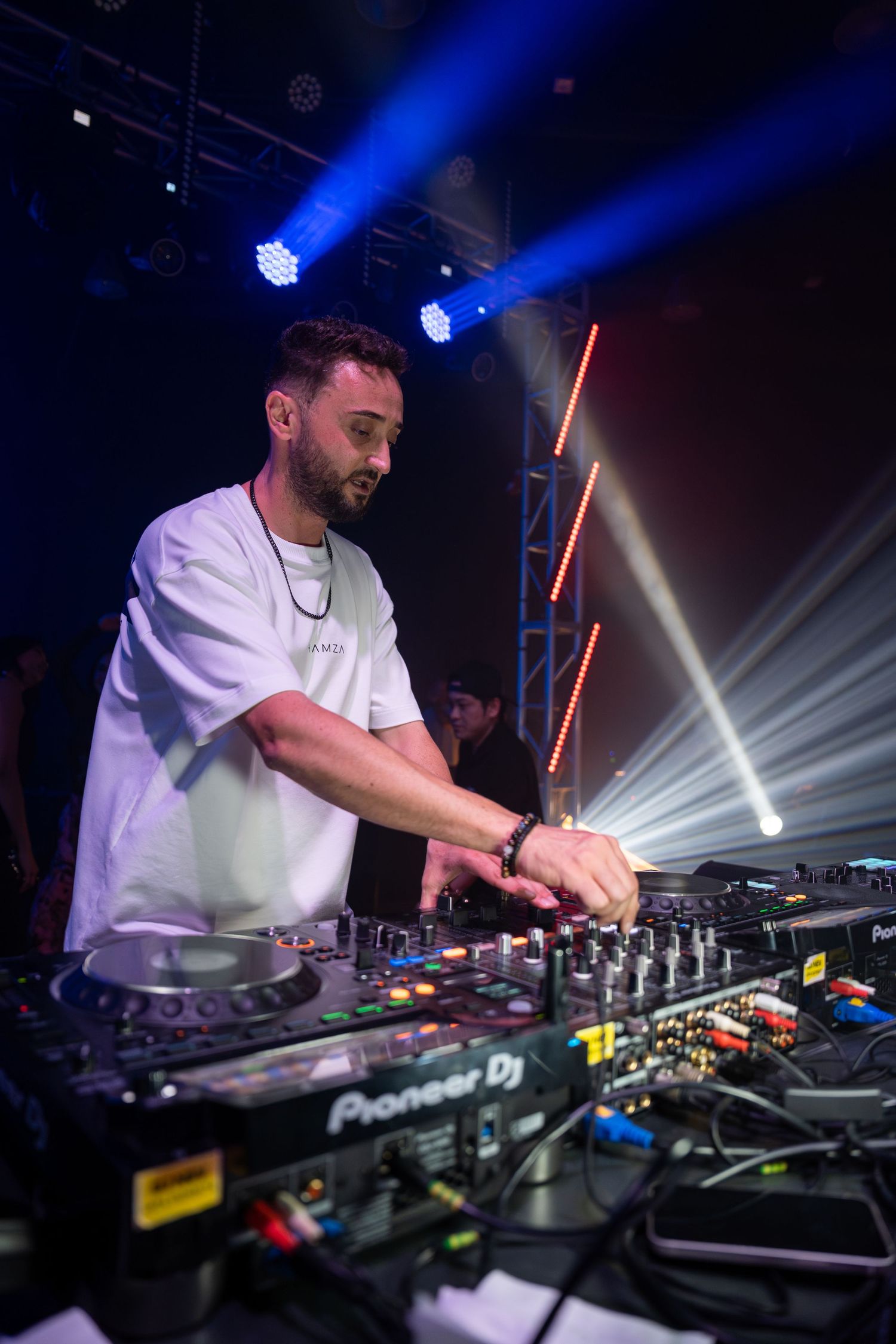 DJ performing on Pioneer DJ equipment under blue stage lights in a dark nightclub venue.