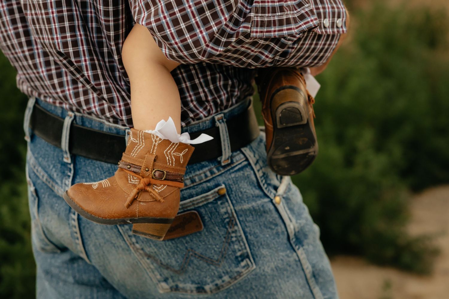 western nebraska family session person in jeans and plaid shirt holding baby in tiny cowboy boots