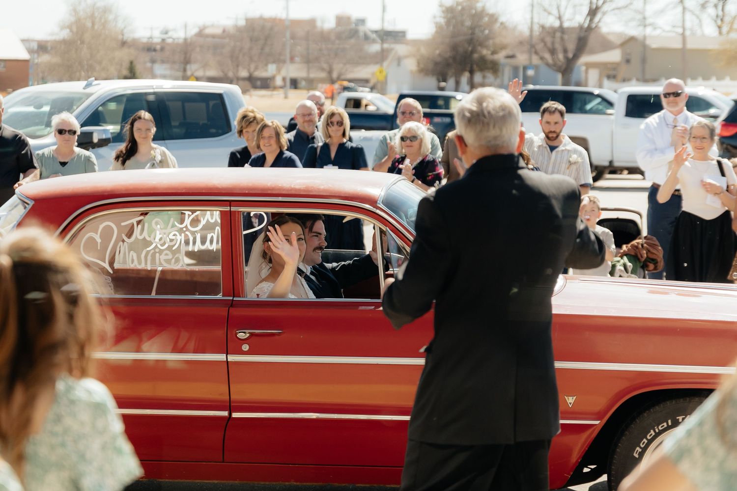 Western Nebraska Wedding Bride and groom depart in a classic red vintage car as wedding guests cheer and applaud