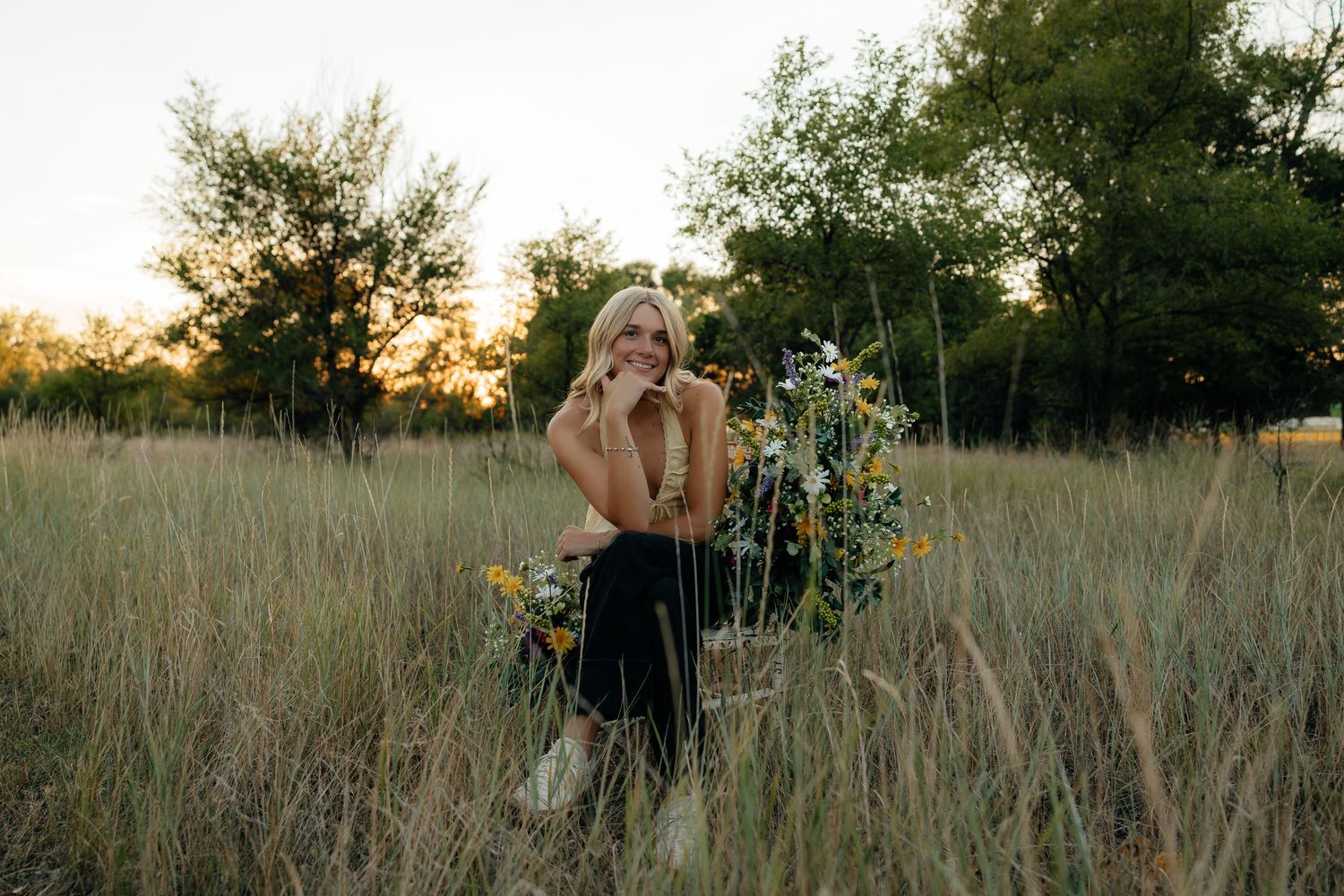 North Platte Nebraska Senior Session girl sitting in tall grass field with wildflowers at golden hour sunset.