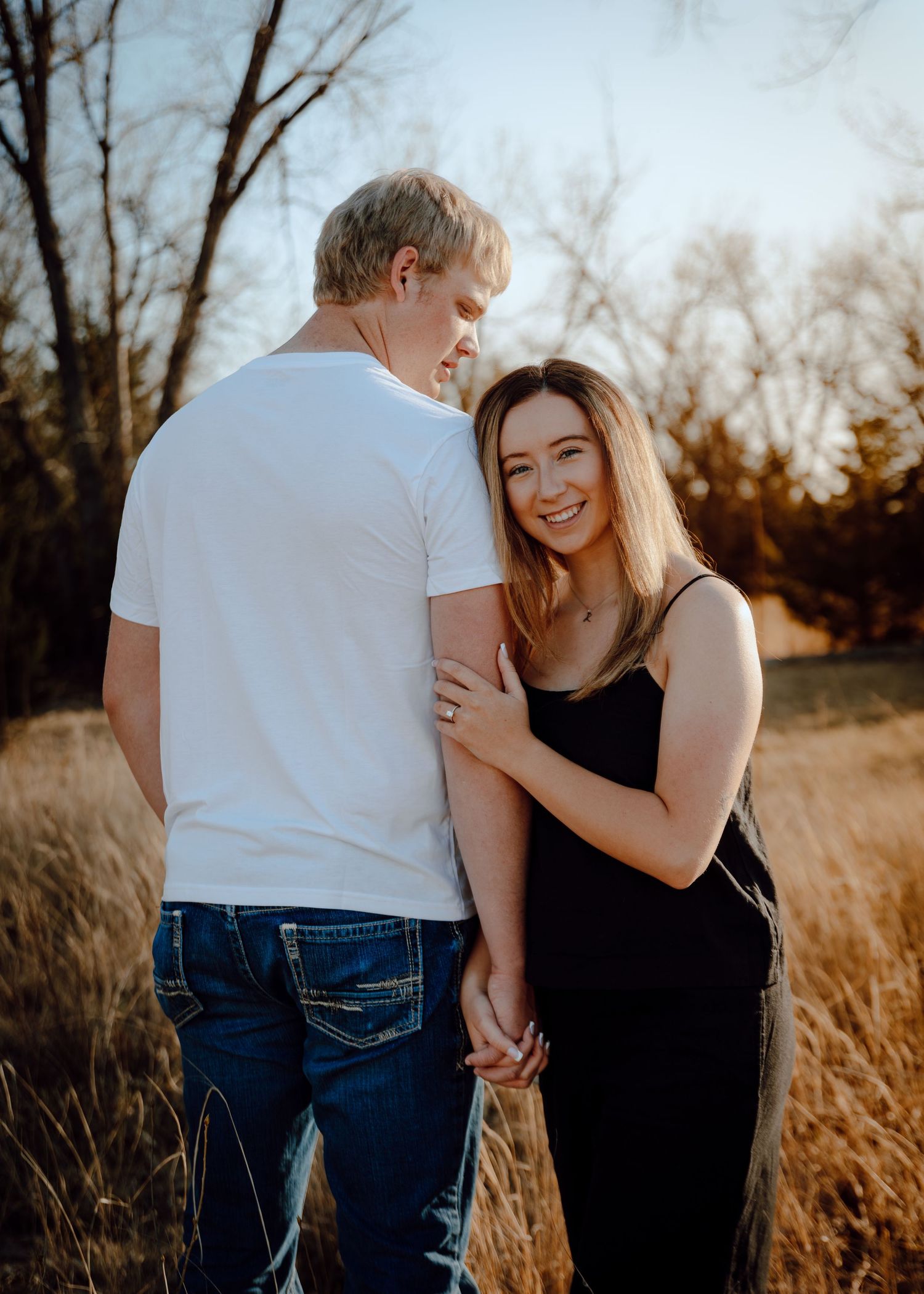 Paxton Nebraska Engagement Session A couple holds hands in a golden field at sunset,