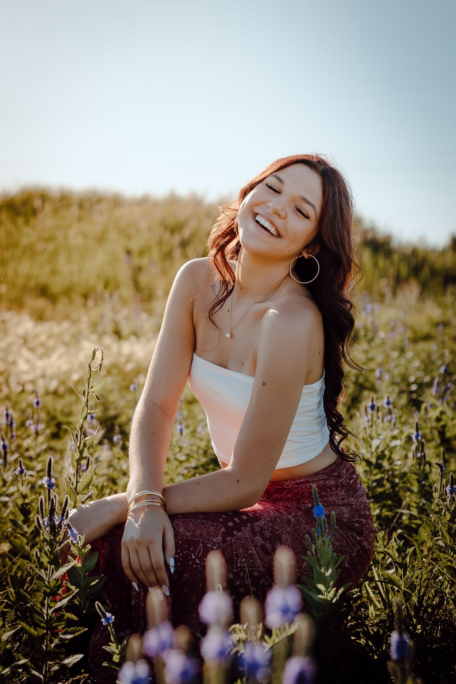 Western Nebraska Senior Session girl laughing in a wildflower field, wearing a white crop top and red skirt on a sunny day.