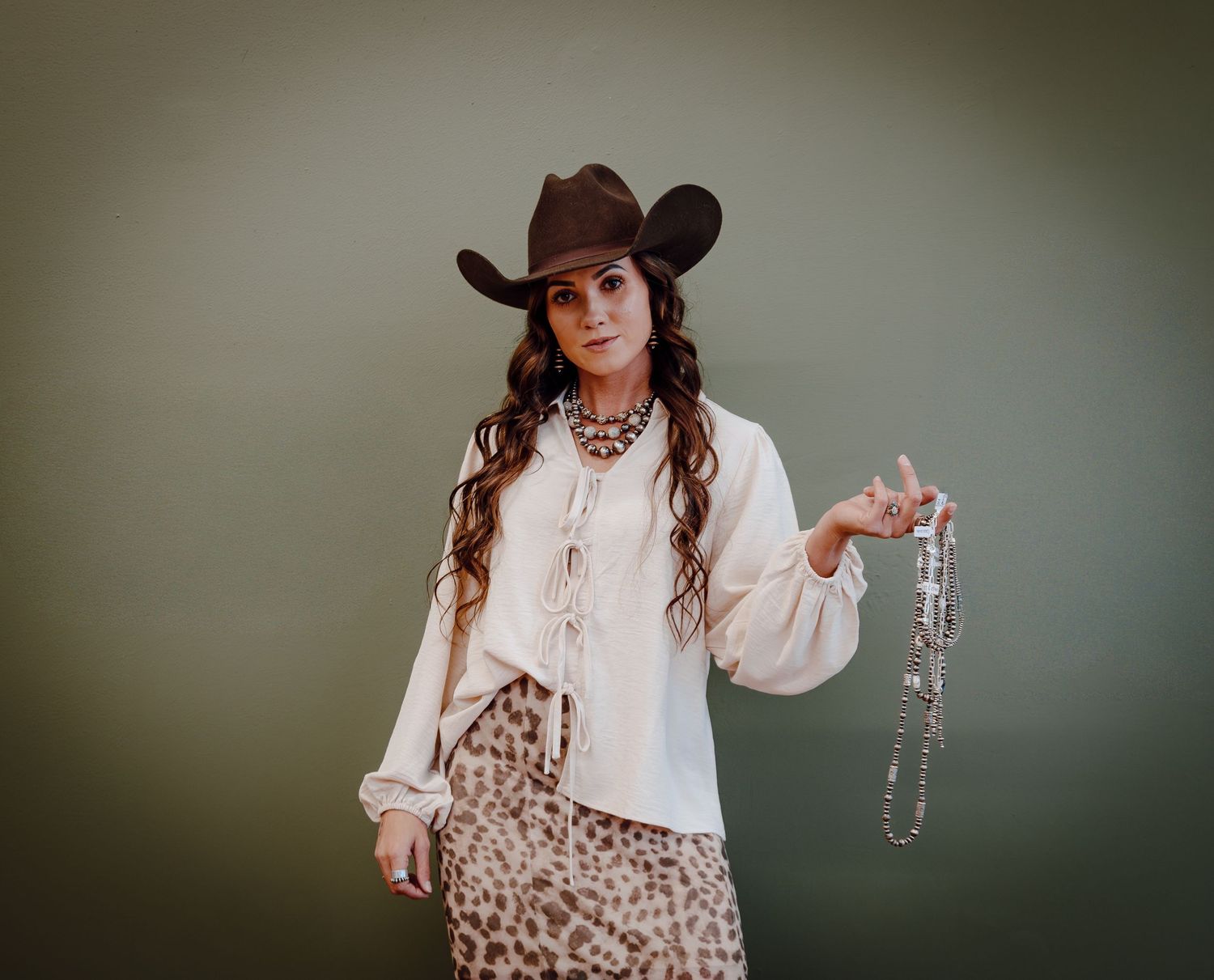 Western Nebraska Brand Session woman in brown cowboy hat and white blouse holds beaded necklaces