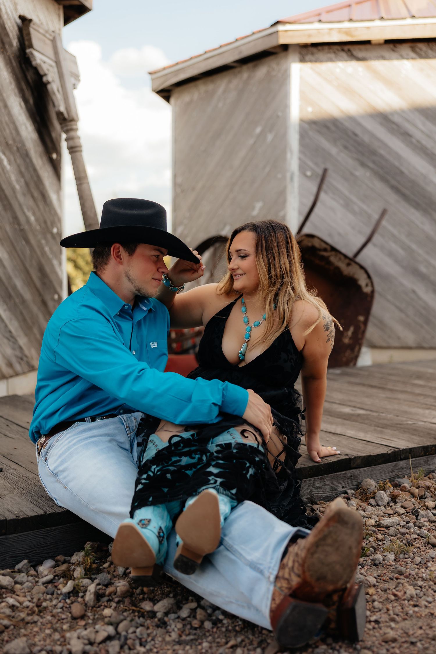 North Platte Nebraska Couples Session couple sits on wooden walkway wearing western attire.
