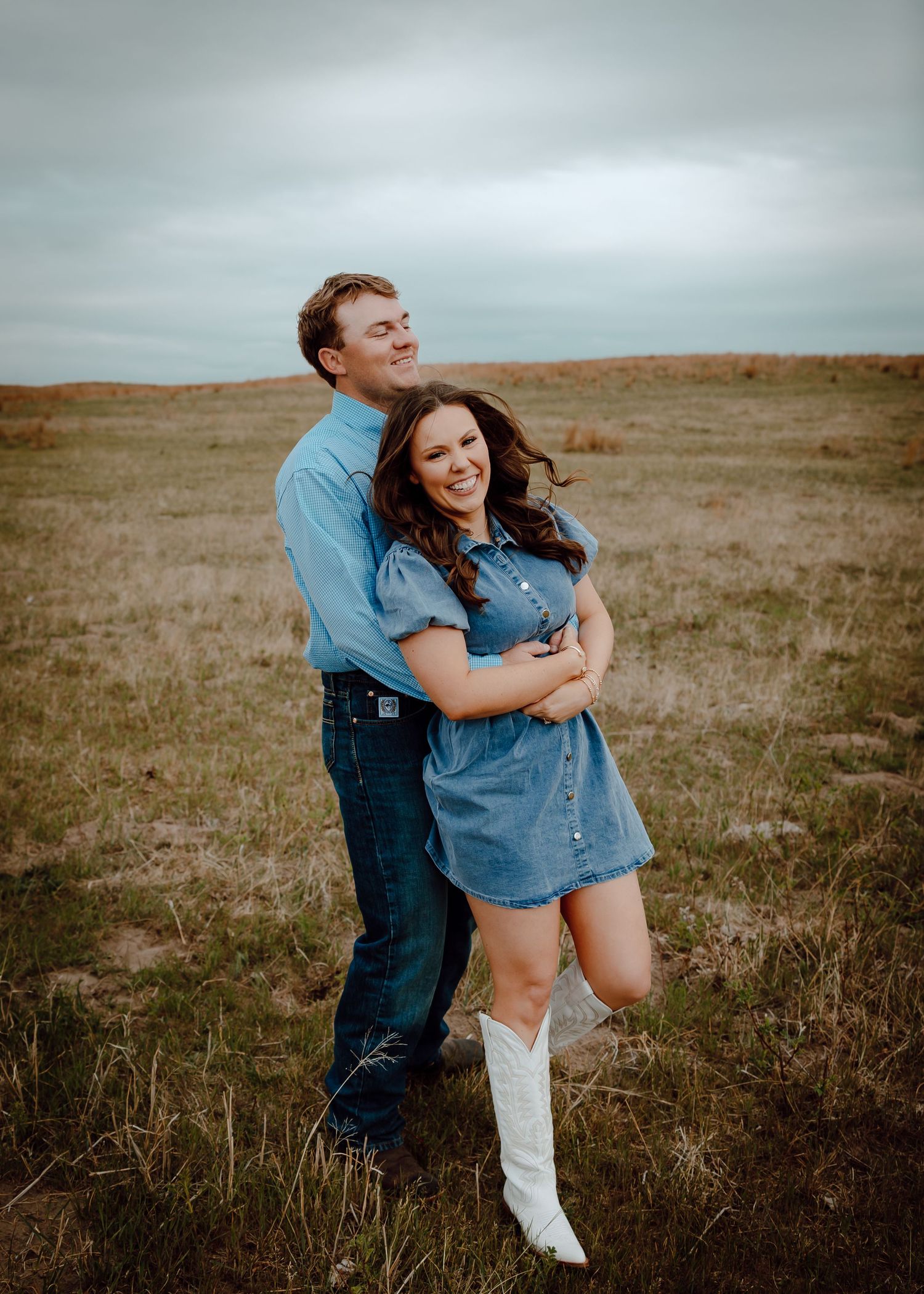 Nebraska Sandhills Engagement Session couple embraces and laughs in an open field wearing cowboy boots and denim