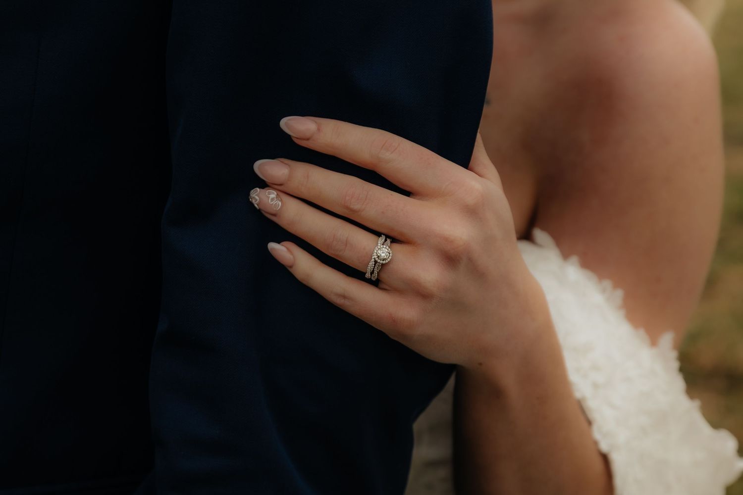 Western Nebraska Wedding Close-up of a bride's hand with wedding and engagement rings resting on groom's navy suit jacket.