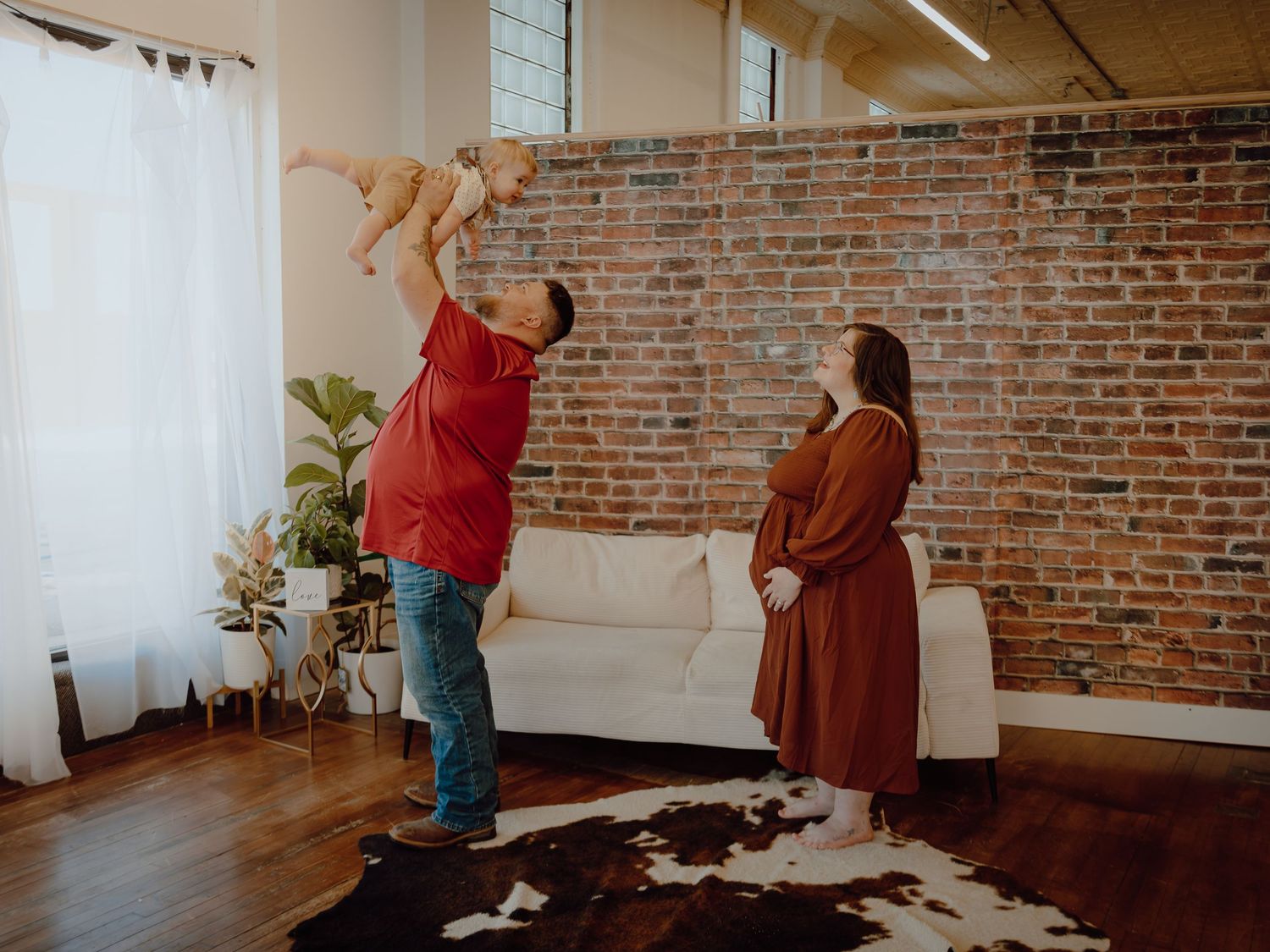 Western Nebraska Family Session A man tosses a baby in the air while a woman watches in a bright studio
