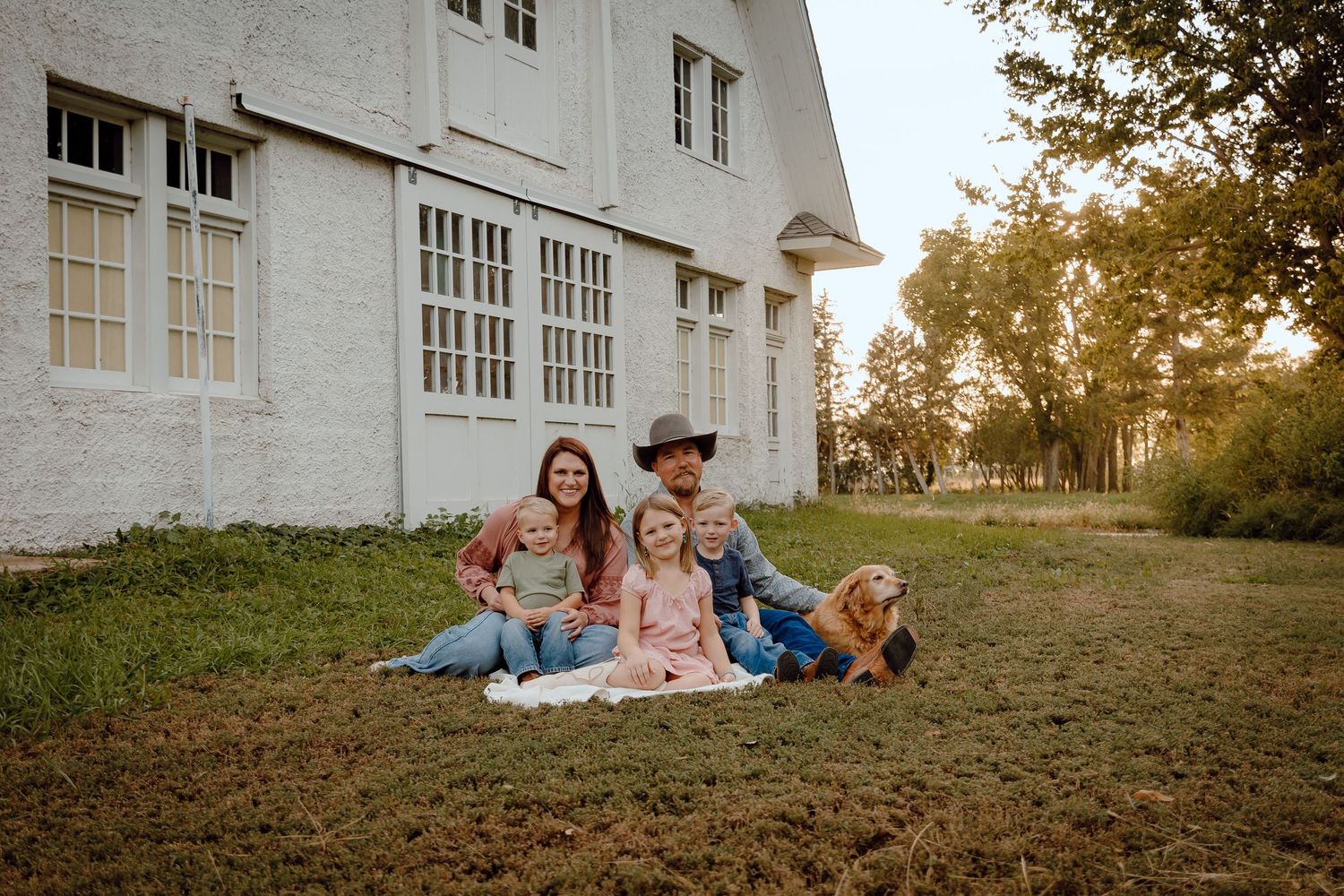 North Platte Nebraska Family Session Family of six poses on grass beside a white barn during golden hour