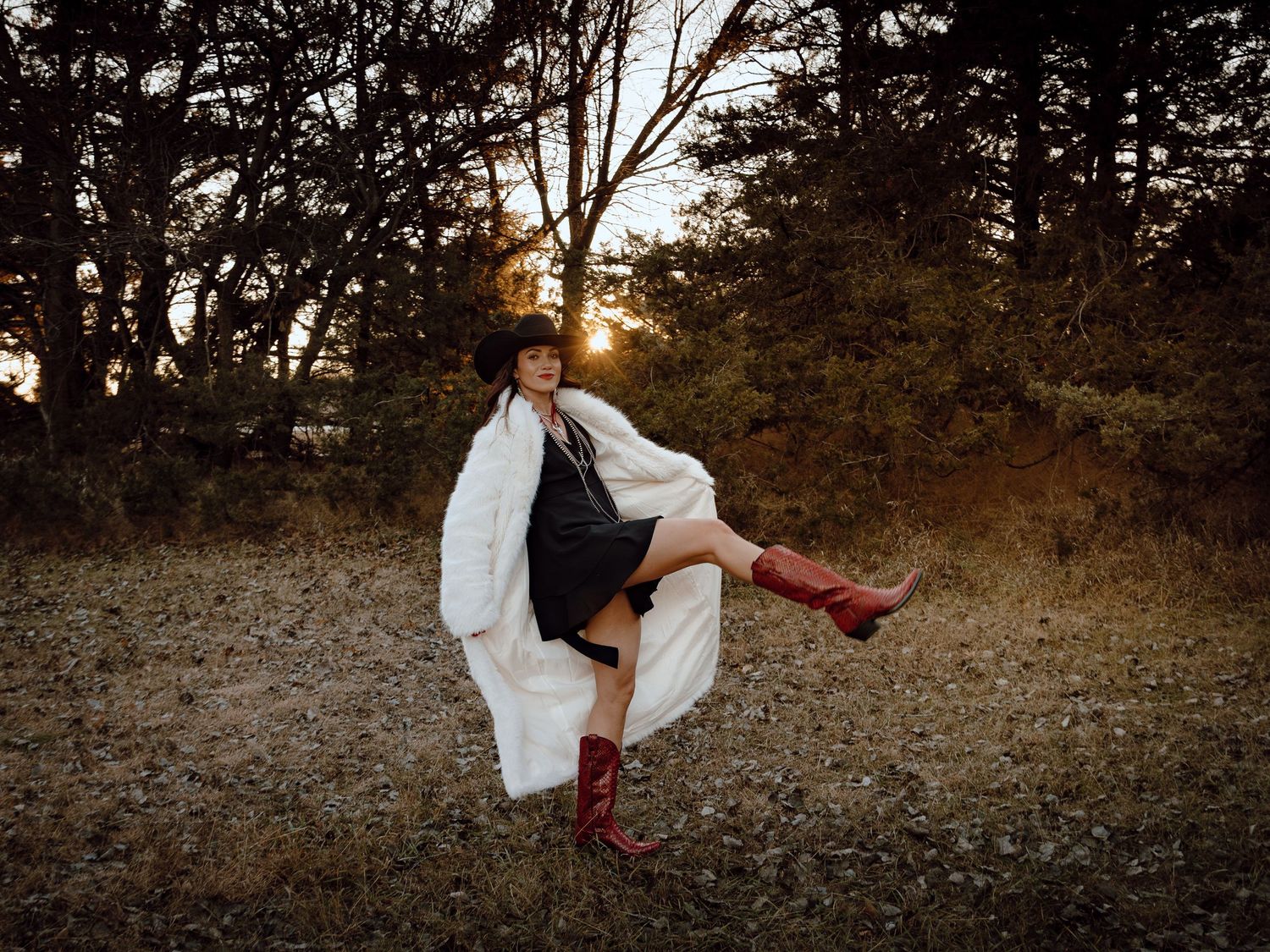 Western Nebraska Brand Session woman in white coat and red boots poses dramatically at sunset