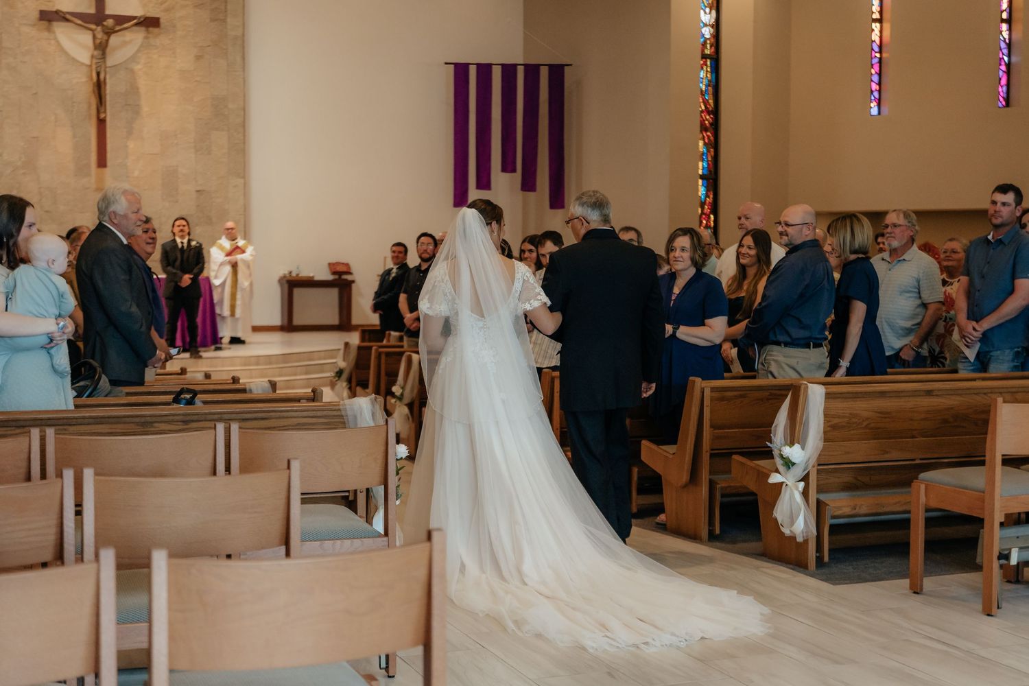 Western Nebraska Wedding Bride in white gown and veil walks down church aisle with her father during wedding ceremony.
