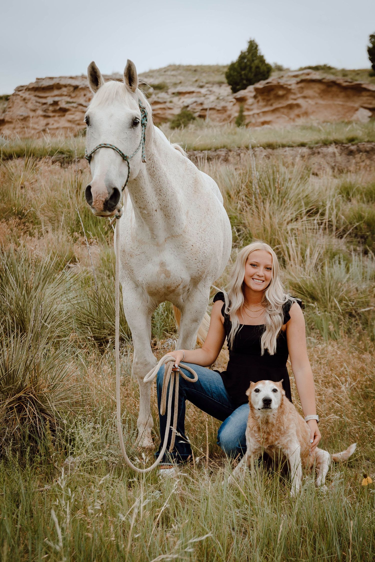 Oshkosh Nebraska senior session  a girl kneels in a pasture with a white horse and red heeler dog against canyon rock