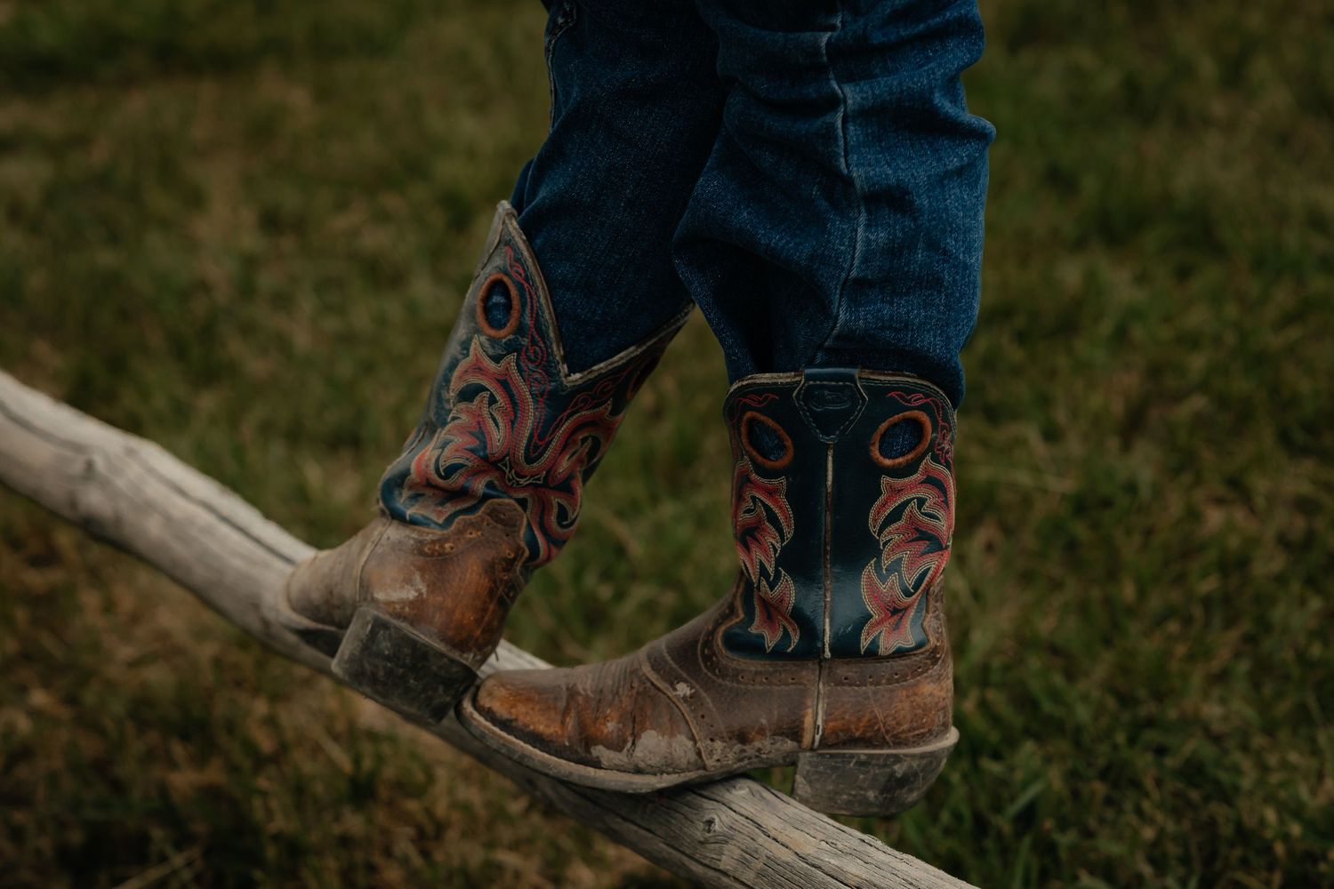 Western Nebraska Family Photography kids brown cowboy boots standing on a wooden fence rail in blue jeans.