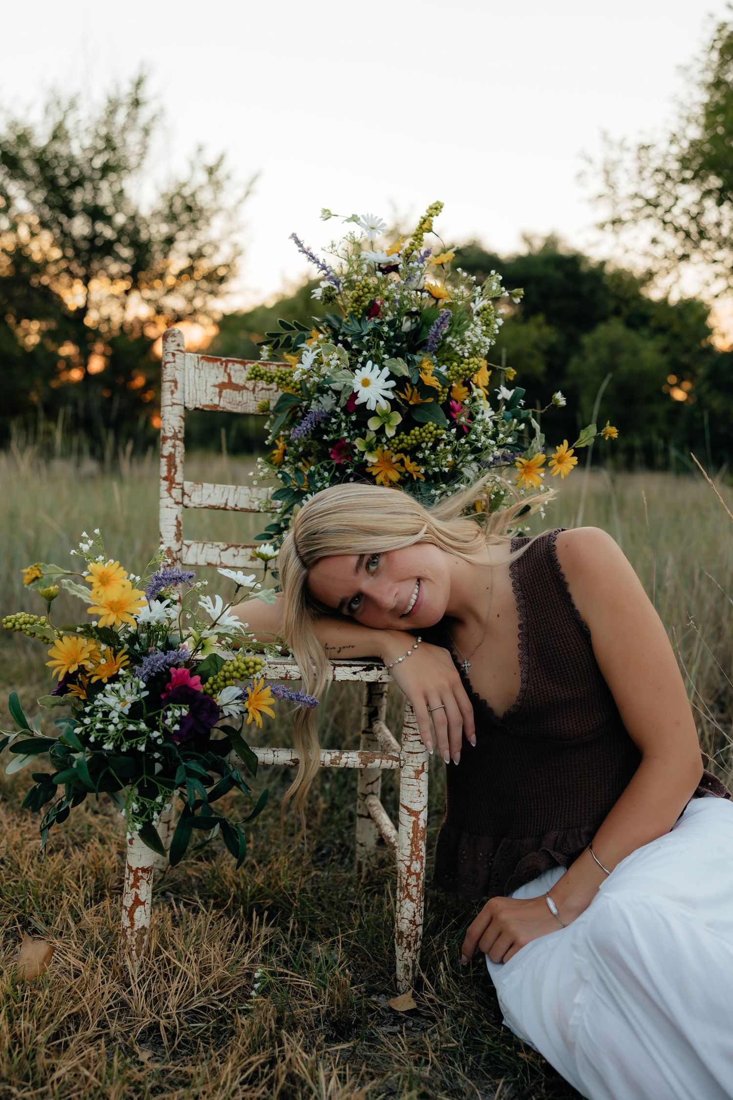 A North Platte Nebraska Senior Session a girl sits in a field with her arm propped on a white floral chair.