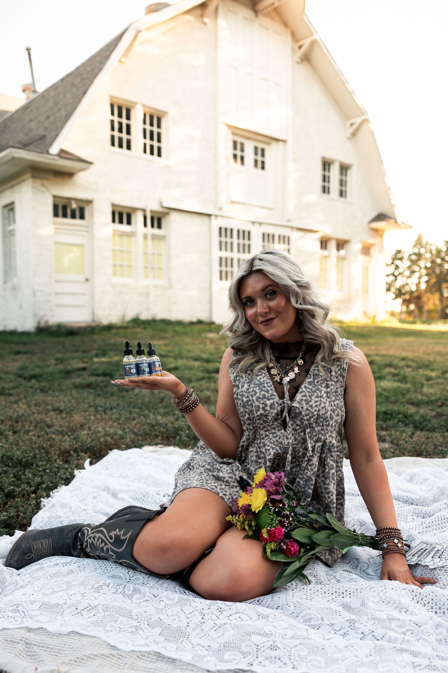 Western Nebraska Brand Session woman in leopard dress holding oil , sitting on lace blanket with flowers,